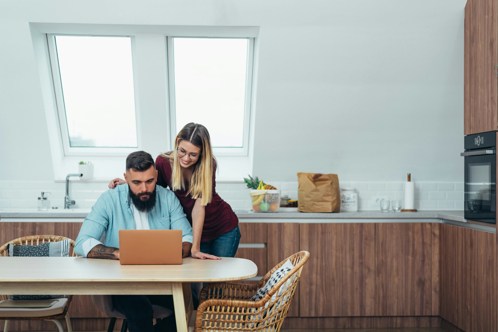 A couple sitting together at a kitchen table, looking at a laptop with warm, hopeful expressions