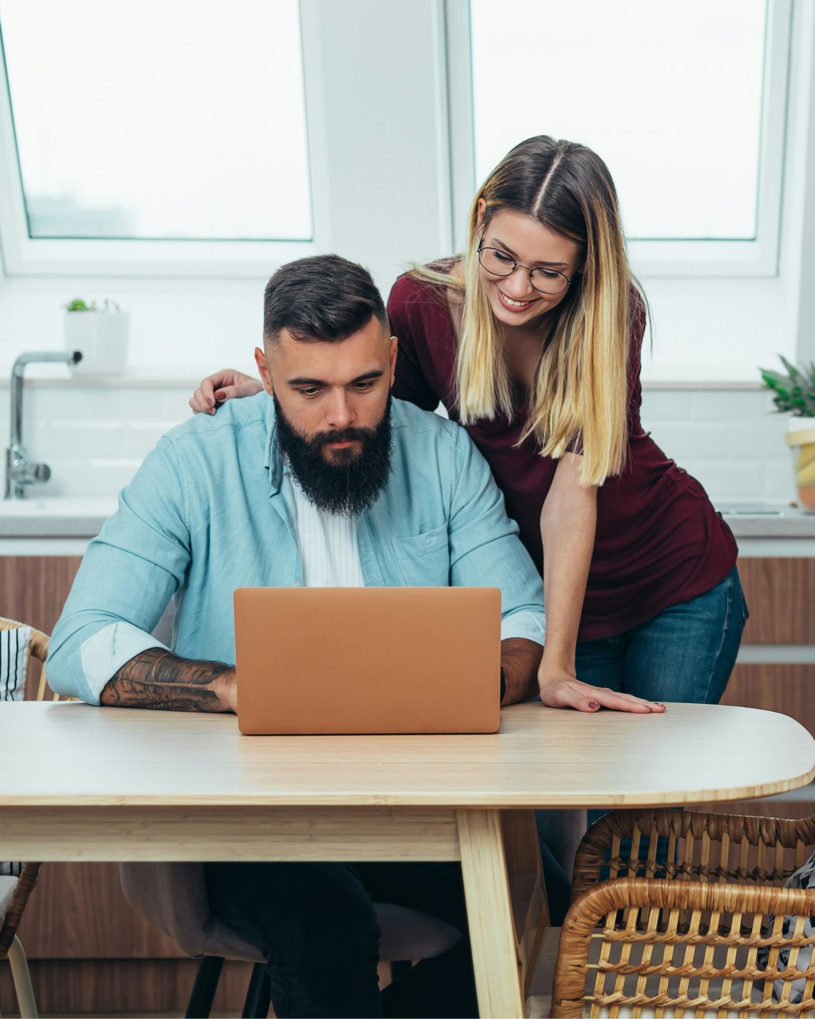 A couple at a kitchen table, looking at a laptop together in bright natural light
